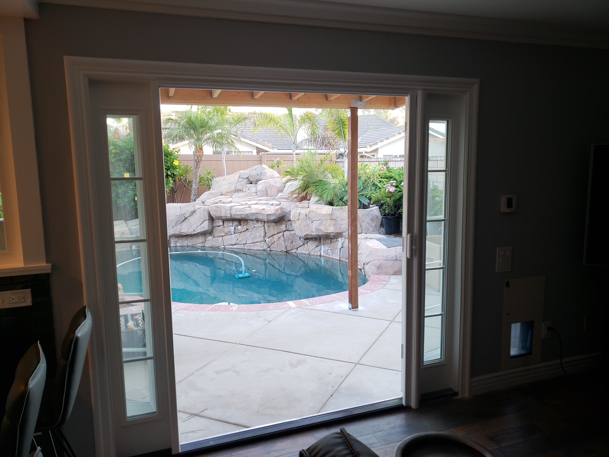 Patio door opening onto a pool backyard with a rock waterfall
